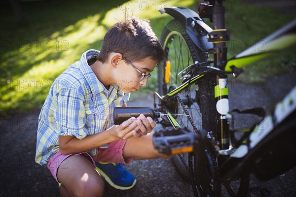 Mixed race boy oiling bicycle chain in backyard