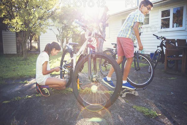 Mixed race children fixing bicycles in backyard