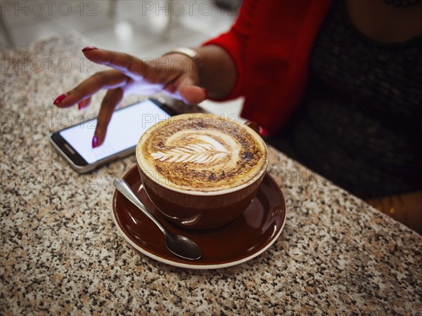 Mixed race woman using cell phone with coffee in cafe