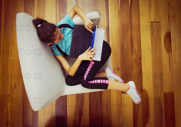 Overhead view of mixed race girl using digital tablet in armchair