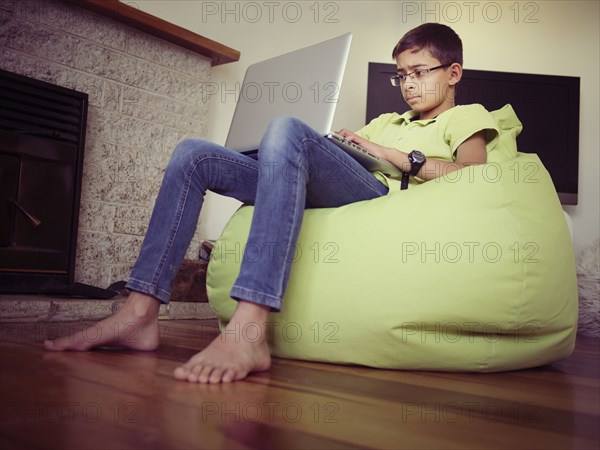 Mixed race boy using laptop in bean bag