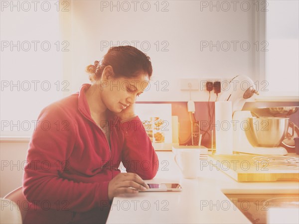 Mixed race woman using cell phone in kitchen