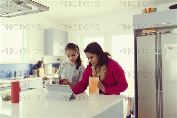 Mother and daughter using digital tablet in kitchen