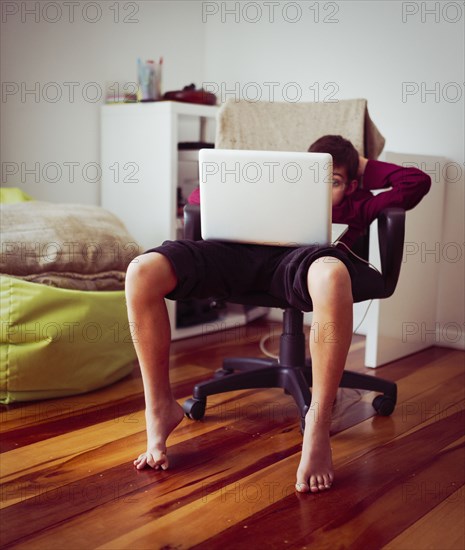 Mixed race boy using laptop in chair
