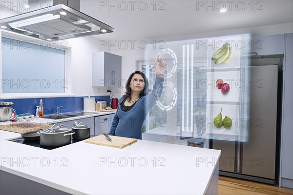 Mixed race woman using holographic screen in kitchen