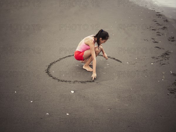 Mixed race girl drawing in beach sand