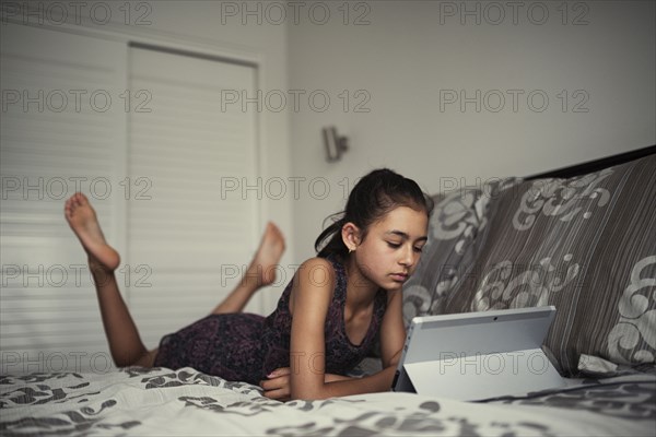 Mixed race girl using digital tablet on bed