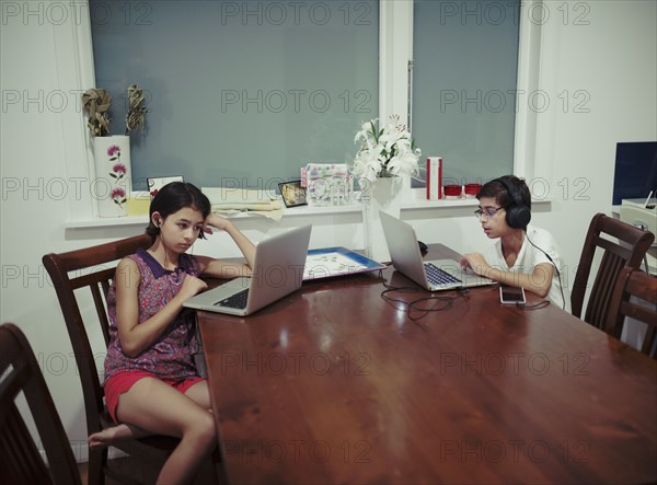 Mixed Race brother and sister using laptops at table