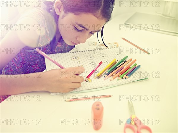 Mixed Race girl drawing faces in notebook