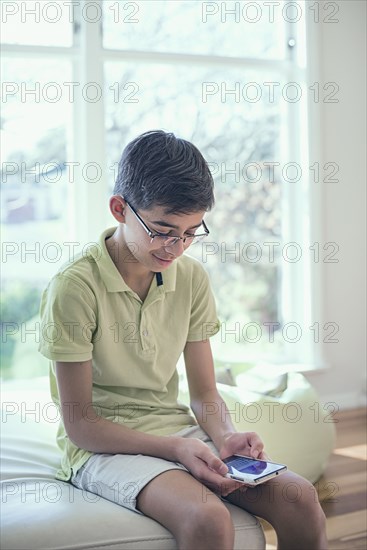 Mixed Race boy texting on cell phone near window