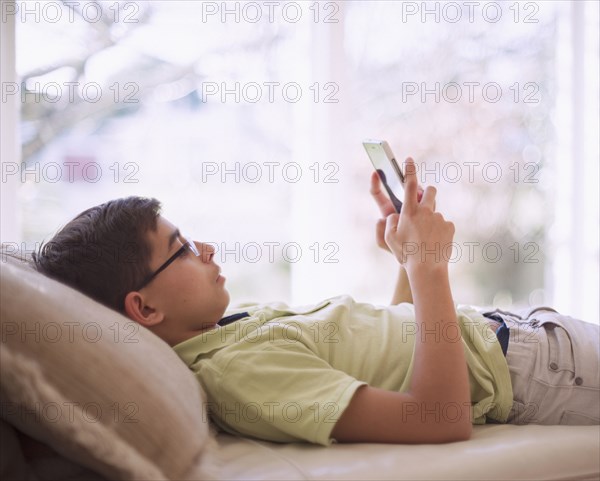 Mixed Race boy texting on cell phone near window