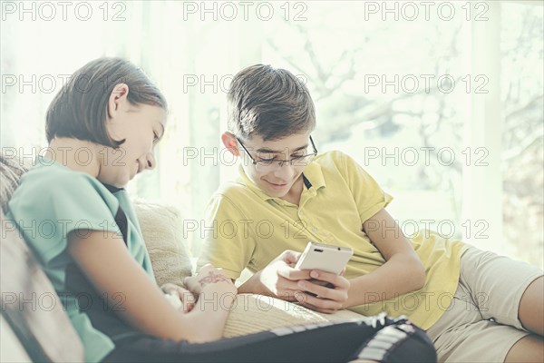 Mixed Race brother and sister texting on cell phone near window