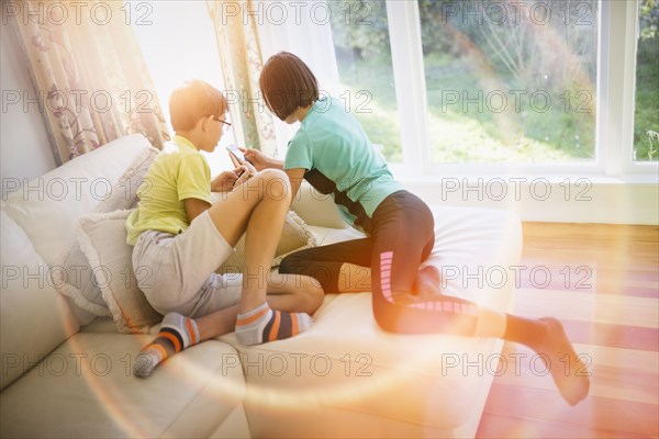 Mixed Race brother and sister texting on cell phone near window