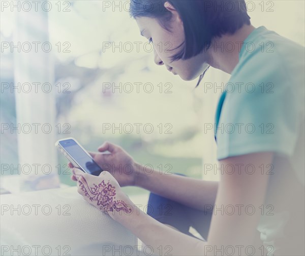 Mixed Race girl texting on cell phone near window