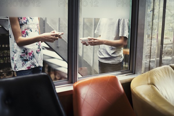 Mixed Race brother and sister texting on cell phones behind window