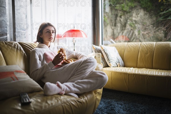 Mixed Race girl wearing rabbit costume sitting on sofa eating croissant