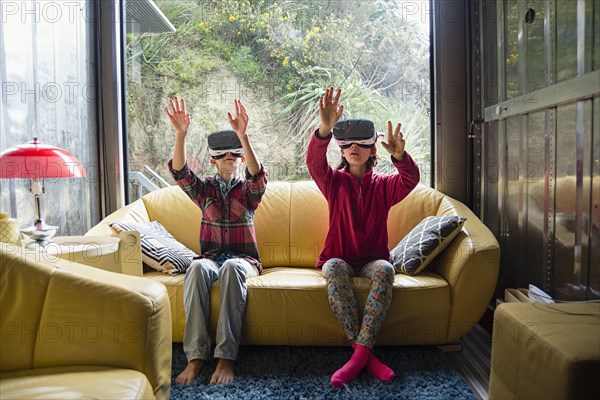 Mixed Race brother and sister using virtual reality goggles on sofa