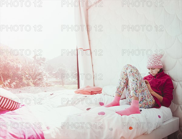 Mixed Race girl sitting on bed texting on cell phone