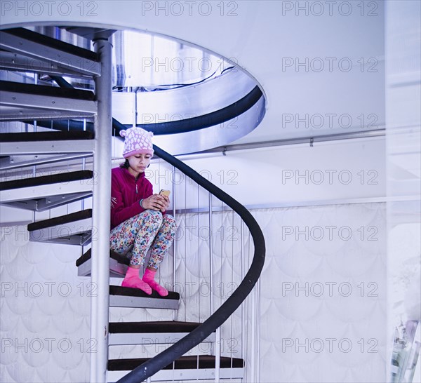 Mixed Race girl sitting on spiral staircase texting on cell phone