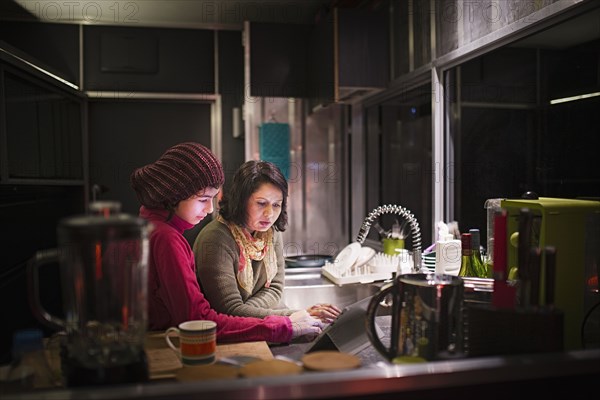 Mother and daughter using digital tablet in kitchen at night