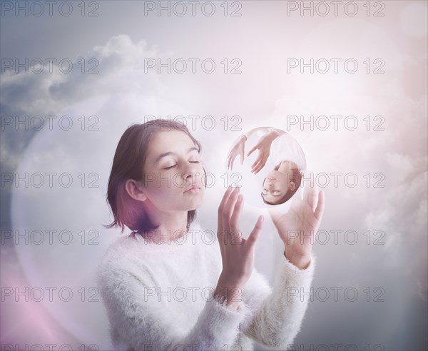 Mixed Race girl in clouds holding glass sphere