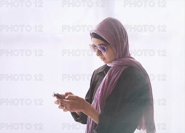 Mixed Race girl wearing heart-shape sunglasses and headscarf texting