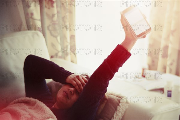 Frustrated Indian woman laying on sofa holding glowing cell phone