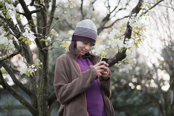 Smiling Mixed Race girl texting on cell phone near tree