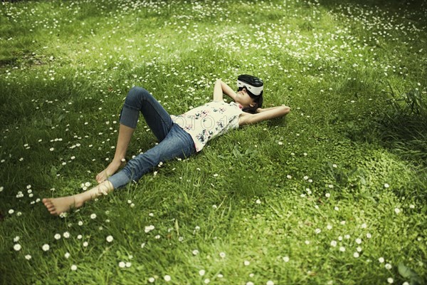 Mixed Race girl laying in grass wearing virtual reality goggles