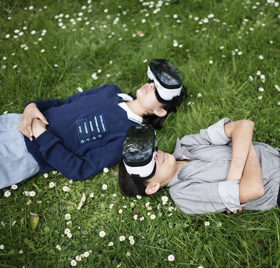 Mixed Race brother and sister laying in grass wearing virtual reality goggles
