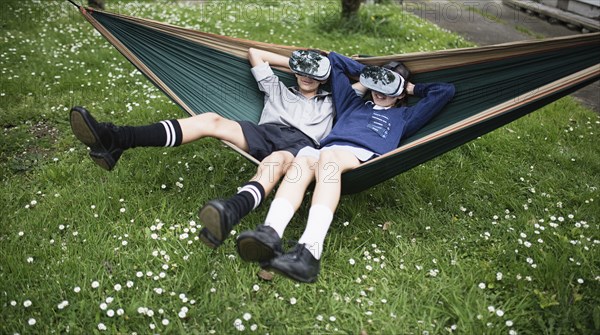 Mixed Race brother and sister in hammock wearing virtual reality goggles