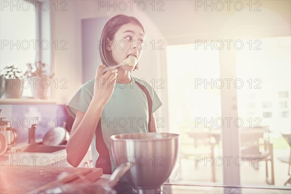Mixed Race girl licking cookie dough on spoon