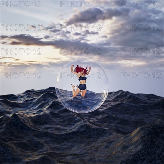 Woman floating in bubble over stormy ocean