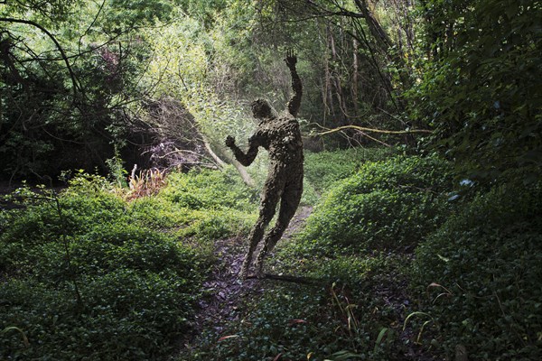 Man covered with rocks with arms raised in forest