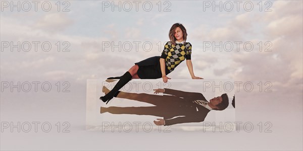 Confident businesswoman sitting on cube with businessman trapped inside