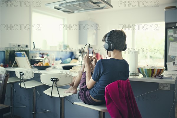 Mixed race boy sitting in kitchen listening to cell phone