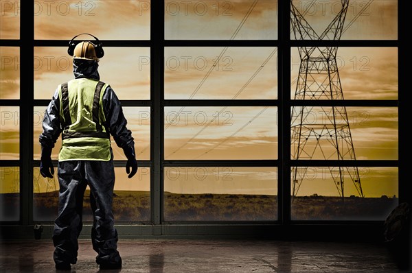 Hispanic construction worker looking out window at power lines