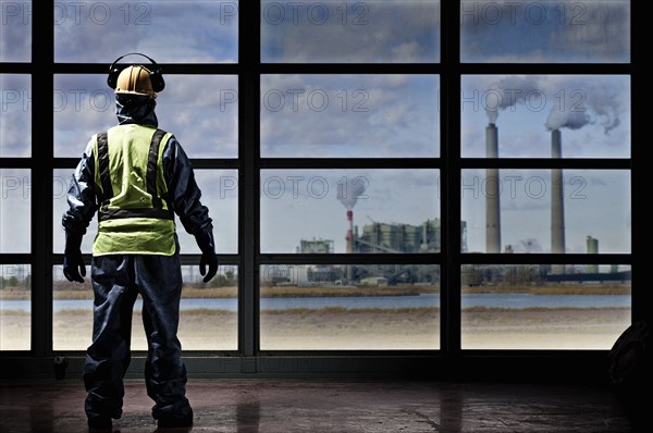 Hispanic construction worker looking out window at factory