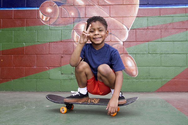 African American boy sitting on skateboard by urban mural