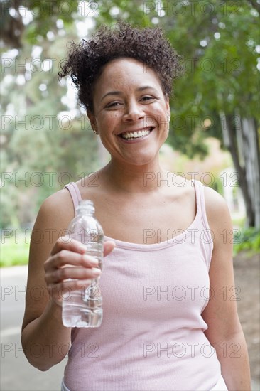Mixed race woman drinking water in park
