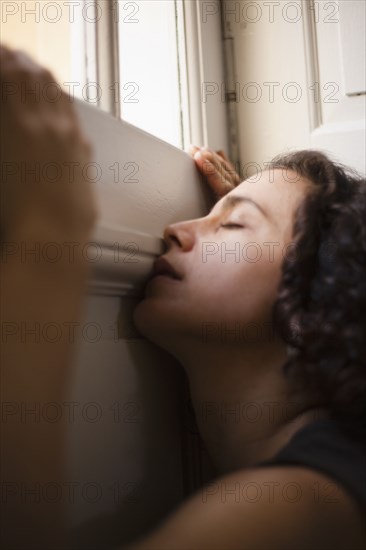 Mixed race woman leaning on wall near window