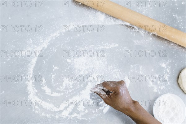 High angle view of baker sprinkling flour on counter