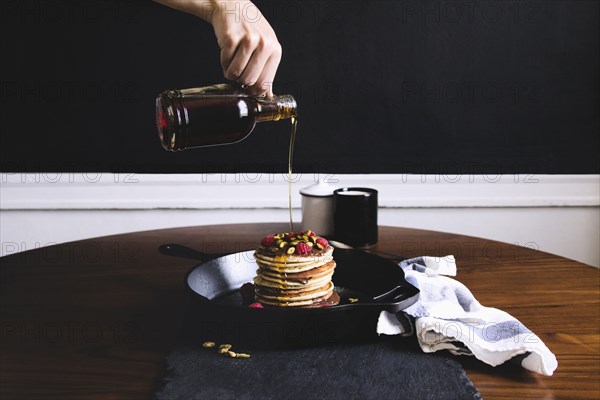 Hand pouring syrup on pancakes