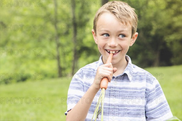 Caucasian boy eating carrot outdoors