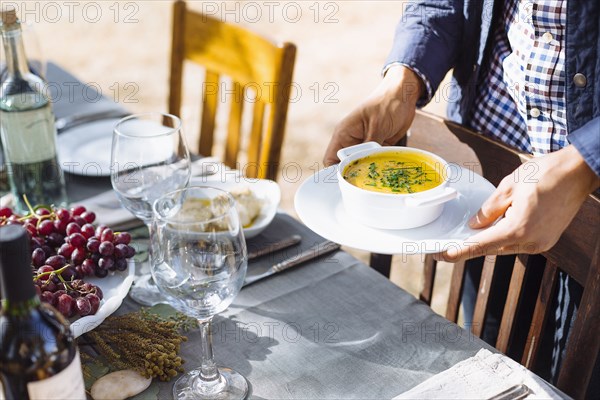 Man setting platter of soup on outdoor table