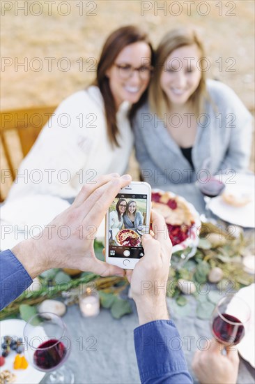 Caucasian man photographing friends at outdoor table