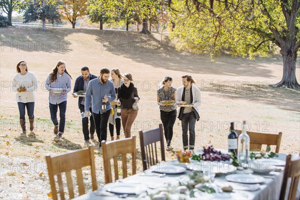 Friends carrying food to outdoor table in rural field