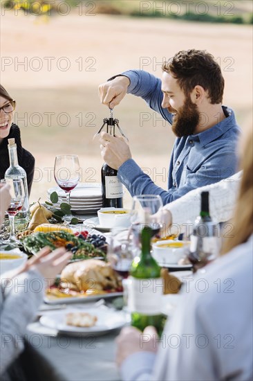 Man opening bottle of wine at outdoor table