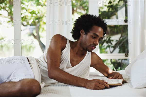 Mixed race man laying on bed reading