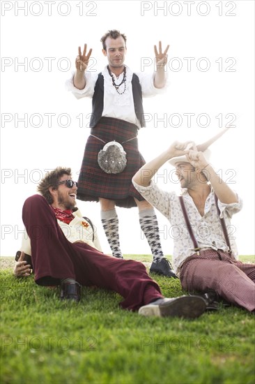 Caucasian man in kilt holding out six fingers to friends